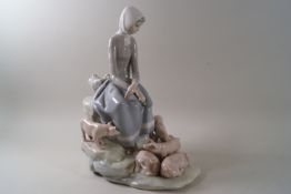 A Lladro porcelain figure of a girl seated on rocks with five piglets at her feet.