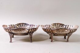 A pair of shaped oval silver dishes with pierced decoration, raised on four legs, London 1925,