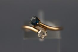 A yellow metal crossover ring with a round faceted cut sapphire and a round rose cut diamond.