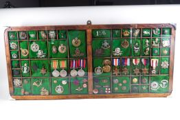 A fitted glazed frame with a collection of war medals and cap badges, including 17/21st Lancers,