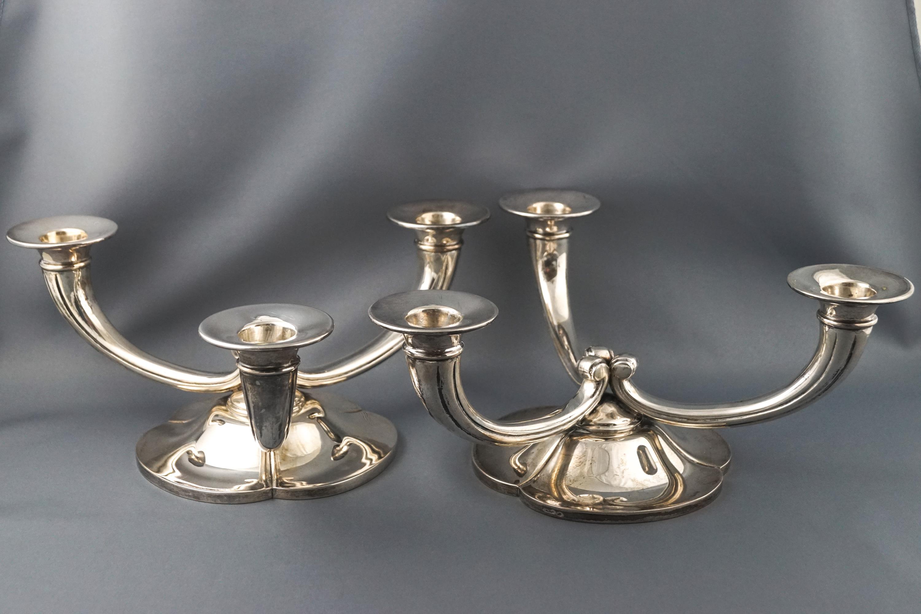 A pair of white metal three branch candelabra with scroll arms on a trefoil floral base,