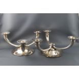 A pair of white metal three branch candelabra with scroll arms on a trefoil floral base,