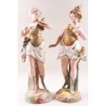 A pair of German porcelain bisque figures of ladies, one with wings, the other helmet and sword,