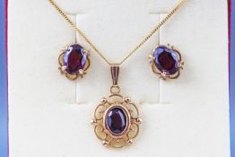 A yellow metal scroll pendant set with garnet together with a matching pair of stud earrings.