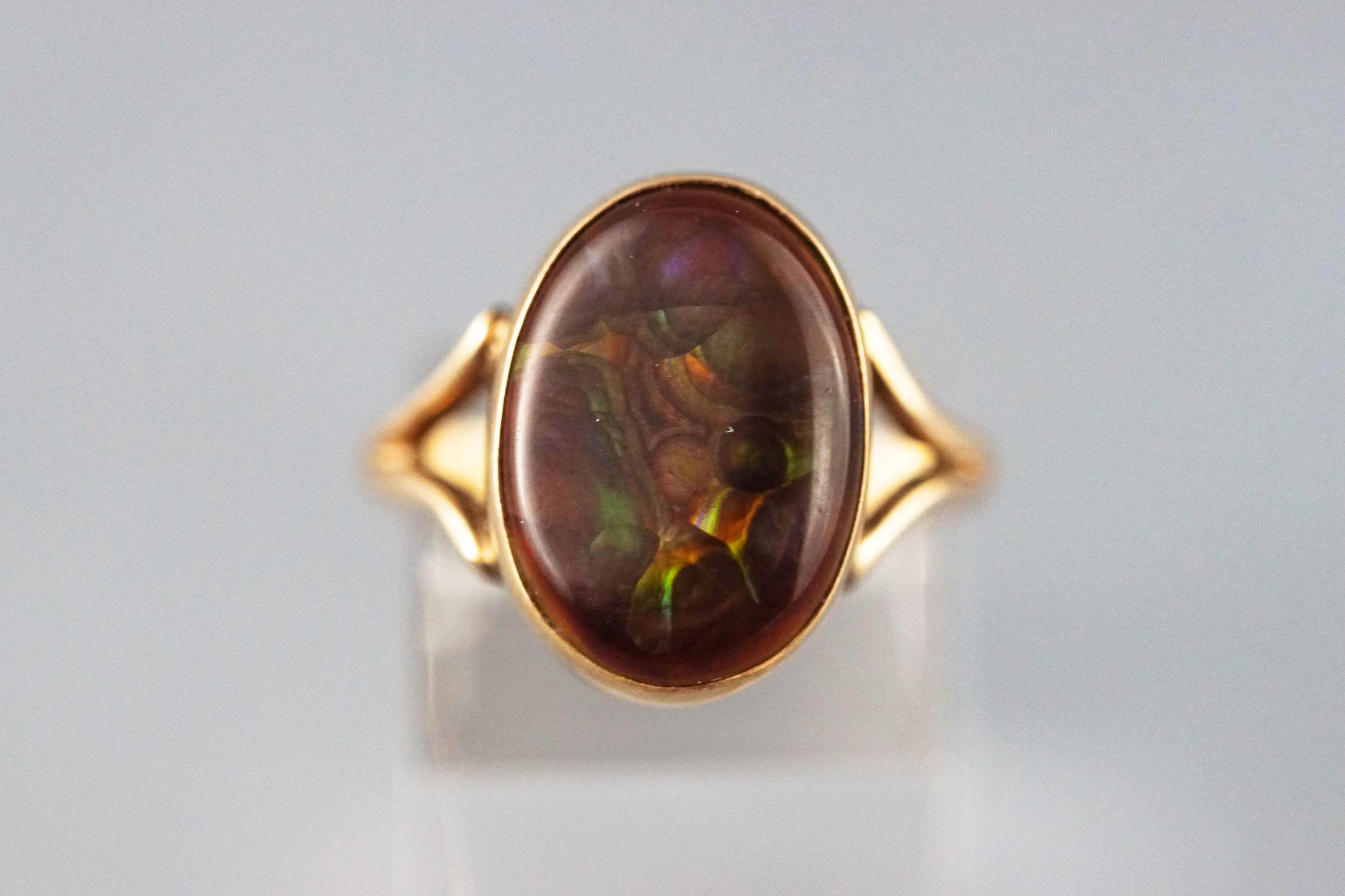A yellow metal single stone ring set with a brown shallow cabochon agate stone measuring 16.