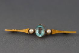 A yellow metal bar brooch set with an oval faceted aquamarine and two seed pearls..