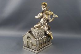 A silver and gilt money box in the form of 'The fiddler on the roof', 16cm high,