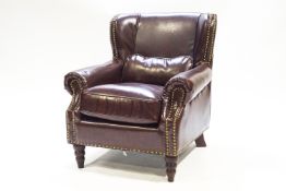 A leather armchair, of club form with over-stuffed arms, raised on mahogany turned legs,
