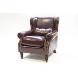 A leather armchair, of club form with over-stuffed arms, raised on mahogany turned legs,