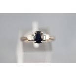 A white metal five stone ring set with an oval faceted cut sapphire.