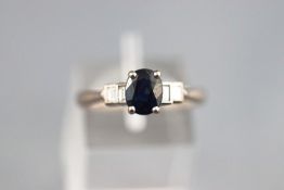 A white metal five stone ring set with an oval faceted cut sapphire.