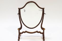 A mahogany swing frame mirror of shield form, on splayed legs,