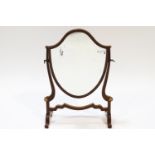 A mahogany swing frame mirror of shield form, on splayed legs,