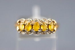 A yellow metal dress ring set with five yellow beryl and diamonds. Hallmarked 9ct gold, Sheffield.