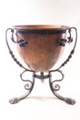 An Arts and Crafts style planter in the form of a copper bowl in a wrought iron stand,