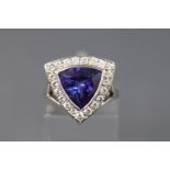 A white metal dress ring set with a triangular faceted cut tanzanite