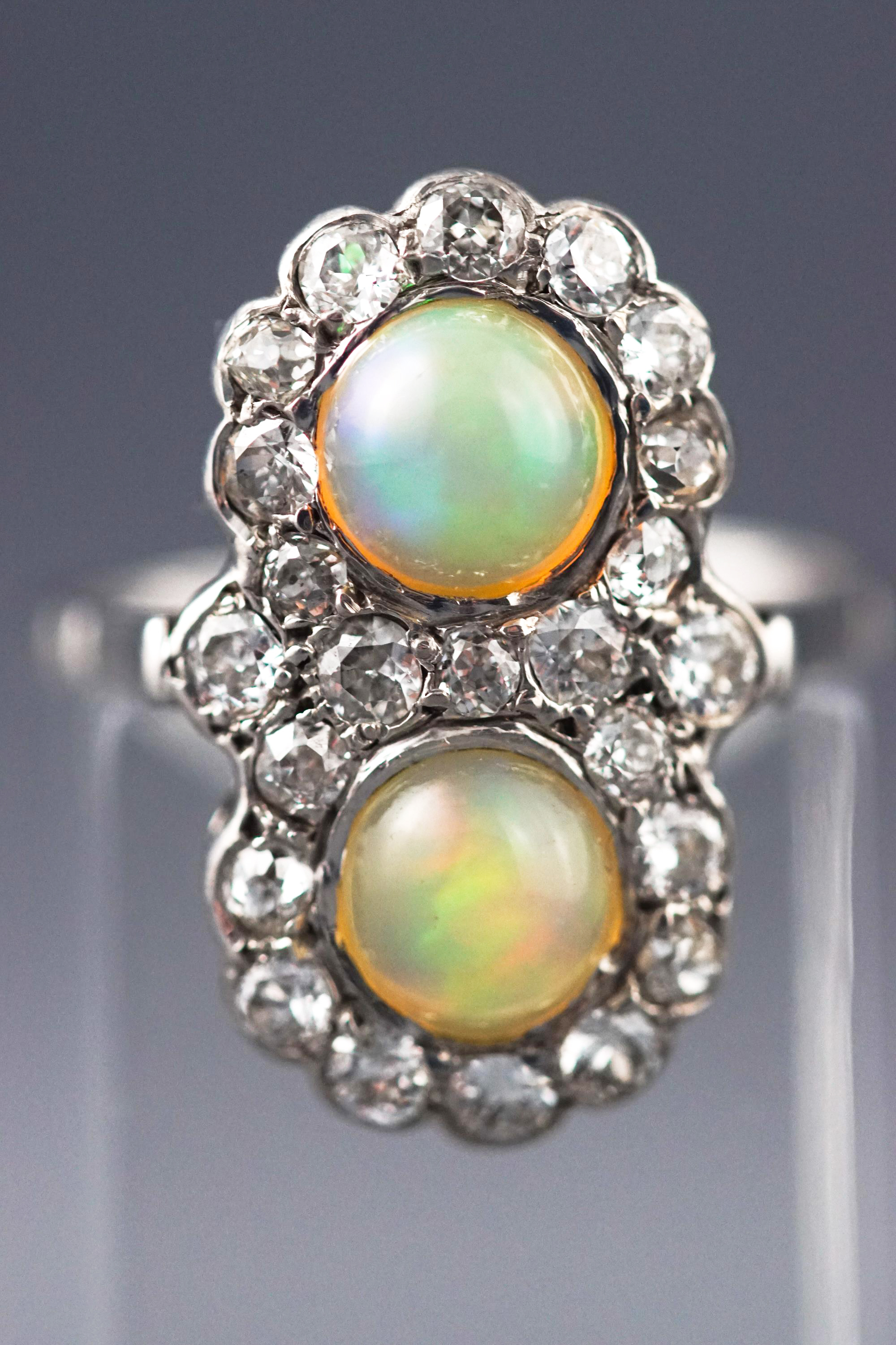 A white metal dress ring set with two circular cabochon opals together with twenty three diamonds.