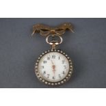 A open face fob watch with blue enamel finish and seed pearls fixed to a 9ct gold bow brooch.
