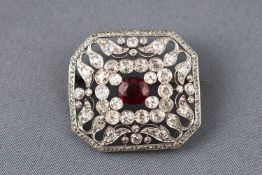 A white metal abstract brooch centrally set with an oval faceted ruby and surrounded by diamonds.