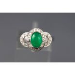 A white metal ring set with a cabochon green dyed jadeite together with grain set diamonds.
