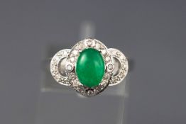 A white metal ring set with a cabochon green dyed jadeite together with grain set diamonds.