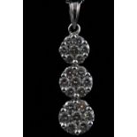A white metal graduated three flower drop cluster pendant set with round brilliant cut diamonds.
