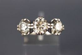A white metal diamond ring set with three graduated round brilliant cut diamonds,