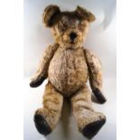 A large plush covered teddy bear, with replacement leather pads to his paws,
