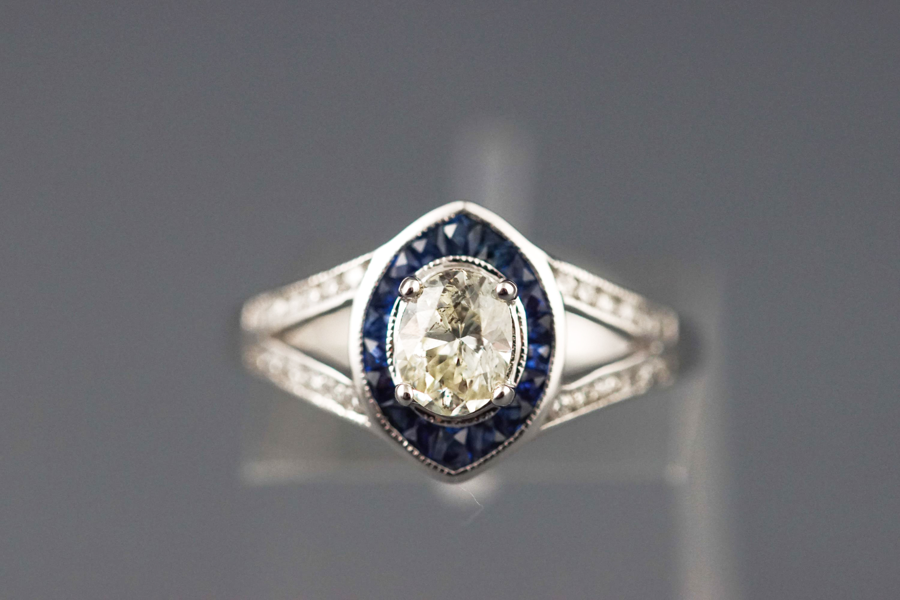 A white metal cluster ring set with a central oval brilliant cut diamond.