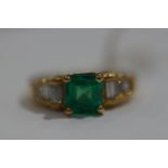 A yellow metal dress ring set with a square emerald together with baguette cut diamond shoulders.