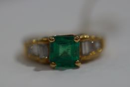 A yellow metal dress ring set with a square emerald together with baguette cut diamond shoulders.