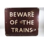 A 'Beware of the Trains' enamel sign on a brown ground,