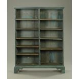 A painted open bookcase, blue, with adjustable shelves and all raised on bracket feet.