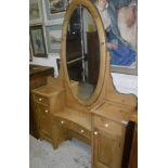 A pine dressing table with oval mirror on a base of various drawers and cupboard doors