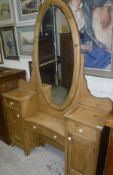 A pine dressing table with oval mirror on a base of various drawers and cupboard doors