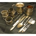 A bag of assorted silver wares to include a set of five napkin rings, two mugs, various cutlery,