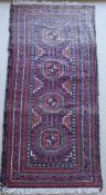 A Turkoman rug, the central panel set with three repeating medallions on a dark red ground,