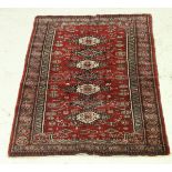 A Bokhara rug, the central panel set with repeating lozenge shaped medallions on a red ground,