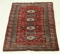 A Bokhara rug, the central panel set with repeating lozenge shaped medallions on a red ground,