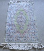 A silk rug, the central panel set with a floral decorated medallion on a green and cream ground,