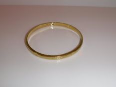 A 585 yellow metal "Slave Bangle" of hollow box form with engraved scrolling floral decoration