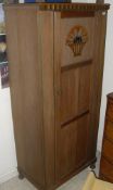 An Arts and Crafts oak single panel door wardrobe and matching cupboard with drawer above cupboard