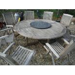 A teak garden table of circular form with eight folding teak chairs by Neptune Classics and a