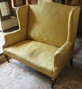 A circa 1900 upholstered wing back scroll arm two seat sofa on square tapered legs to castors