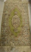 A silk rug, the central panel set with a floral decorated medallion on a green and cream ground,