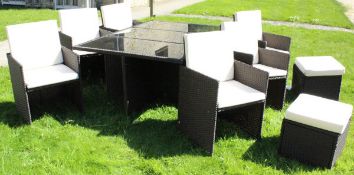 A rattan garden table with smoked glass top and six chairs that fit beneath,