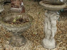 A modern concrete bird bath, the dish supported by the Three Graces on a rocky base,