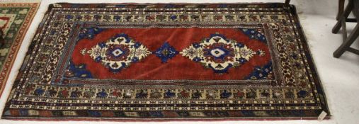 A Caucasian rug, the central panel set with two lozenge shaped medallions on an oxblood red ground,