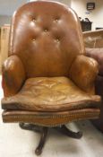 A brown leather upholstered button back swivel chair with brass studded decoration