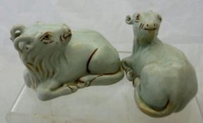 Two Chinese pale celadon glazed figures of recumbent goats with oxide red highlighting,